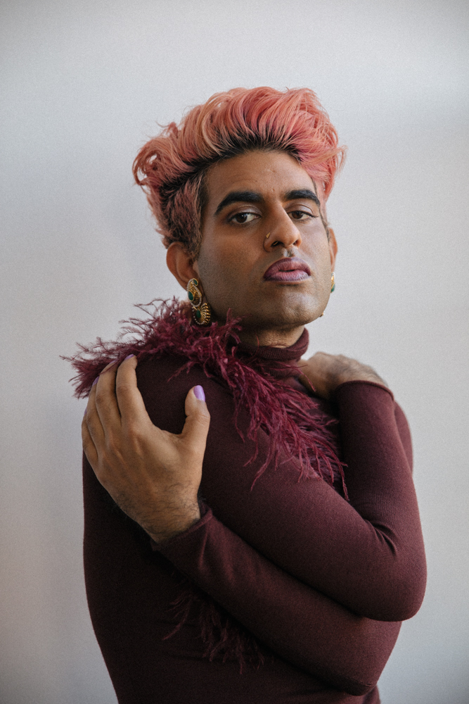 image of alok, a tan person with pink and black short hair, wearing a furry maroon sweater